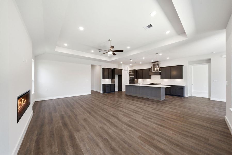 Expansive open-concept living area with tray ceilings, modern fireplace, and seamless flow to the kitchen.