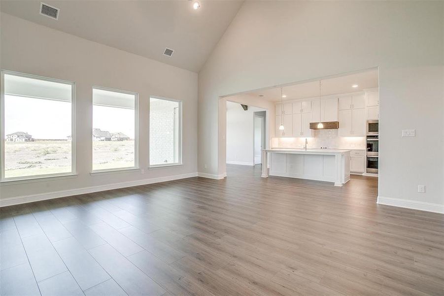 Unfurnished living room with light hardwood / wood-style flooring, high vaulted ceiling, and sink