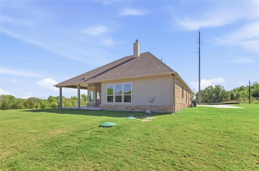 Rear view of property with a yard, a patio area, a chimney, brick siding, and roof with shingles