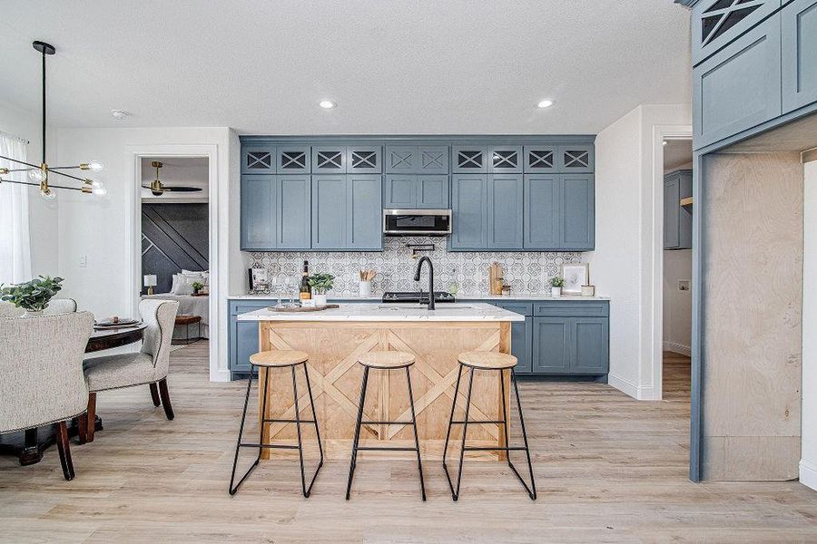 Kitchen featuring light wood-type flooring, a kitchen bar, a center island with sink, stainless steel microwave, and decorative backsplash