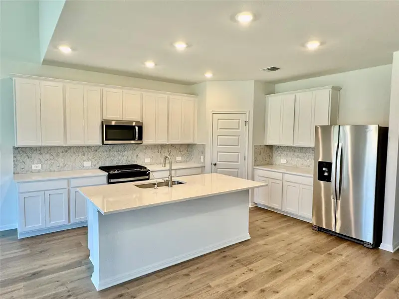 Kitchen featuring stainless steel appliances, white cabinets, light stone counters, light wood-type flooring, and a kitchen island with sink