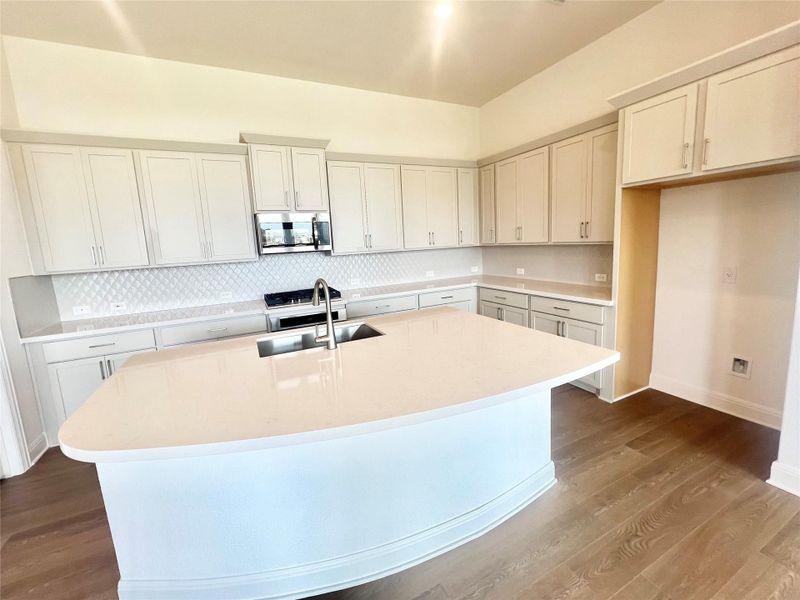 Kitchen featuring a kitchen island with sink, stainless steel microwave, light countertops, and dark wood-type flooring Kitchen featuring a kitchen island with sink, stainless steel microwave, light countertops, and dark wood-type flooring
