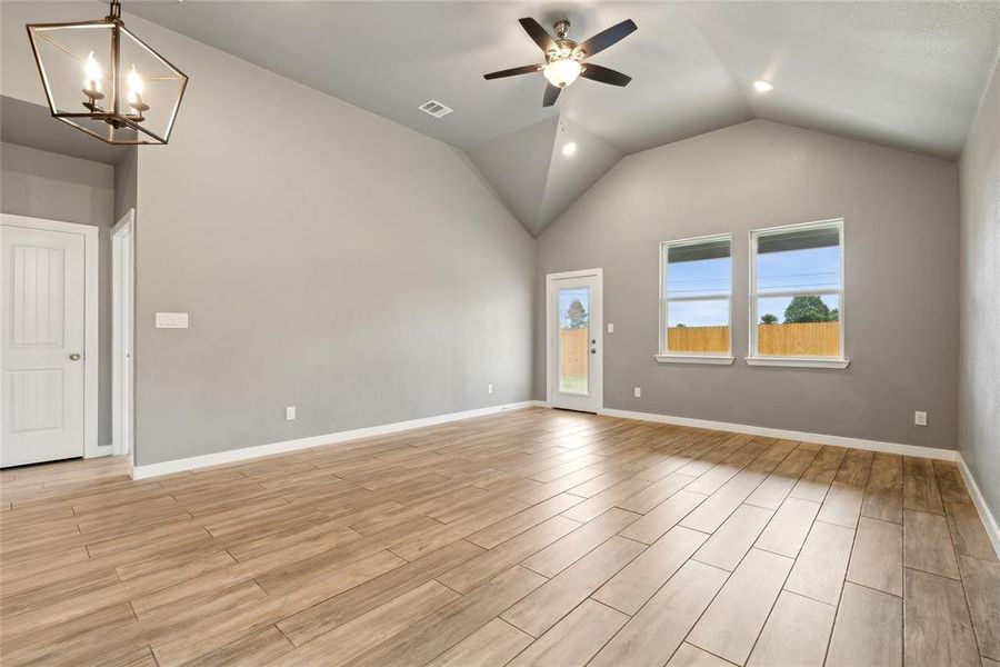 Spare room featuring light wood-type flooring, ceiling fan with notable chandelier, and vaulted ceiling