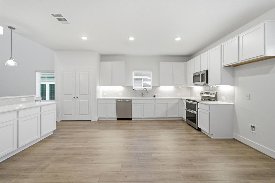 Kitchen featuring white cabinets, stainless steel appliances, decorative light fixtures, and tasteful backsplash