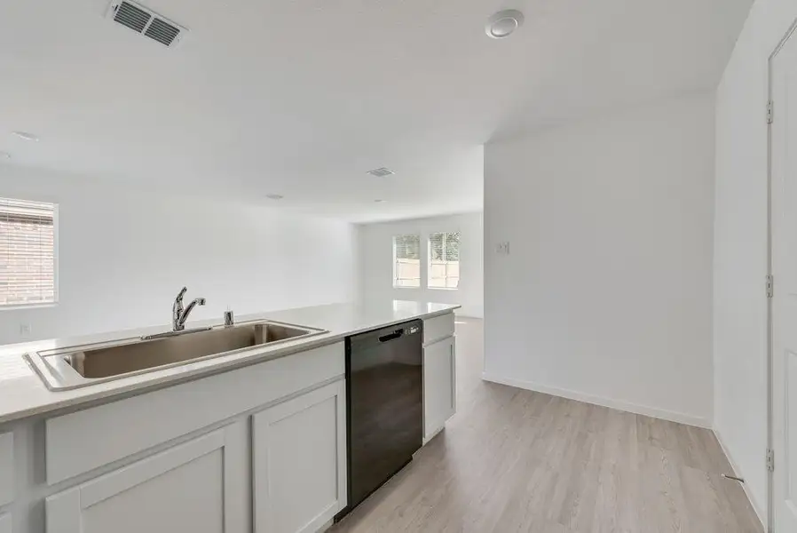 Kitchen with light wood-type flooring, black dishwasher, white cabinetry, and light stone countertops