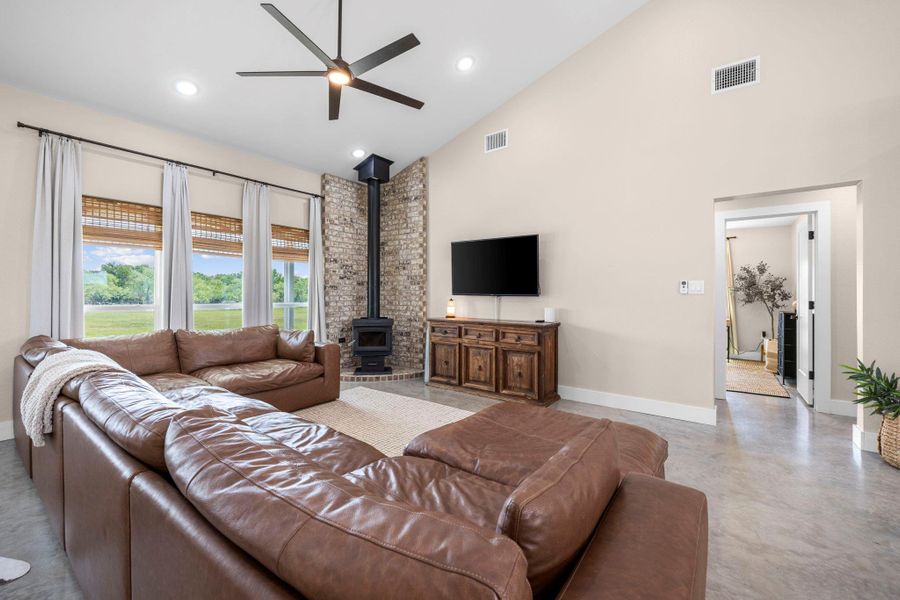 Living room with a wood stove, a ceiling fan, finished concrete flooring, vaulted ceiling, and recessed lighting