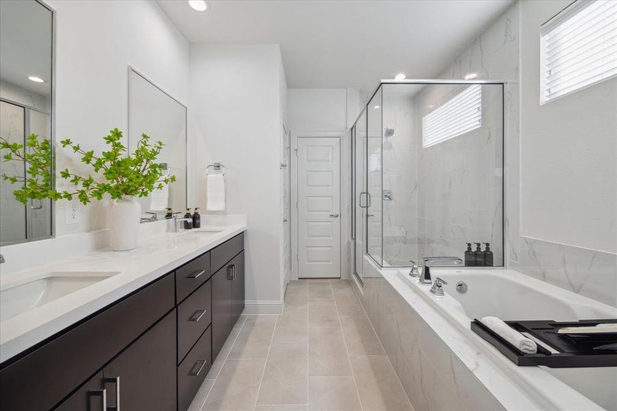 This luxurious primary bathroom offers a spa-like experience with a soaking tub and glass-enclosed walk-in shower. The sleek double vanity provides ample counter space and storage, while the neutral tile and marble finishes create a calming atmosphere.