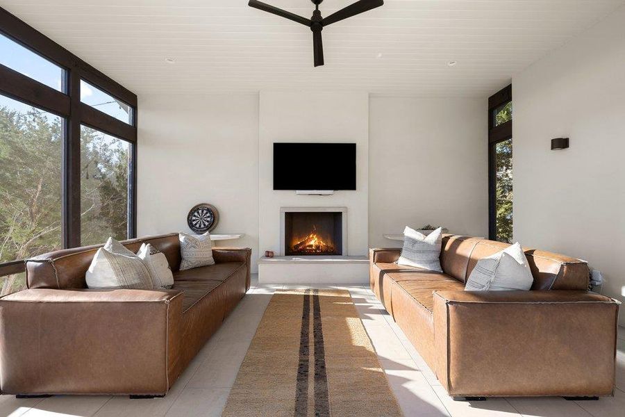 Living area featuring light tile patterned floors, a ceiling fan, a lit fireplace, and healthy amount of natural light