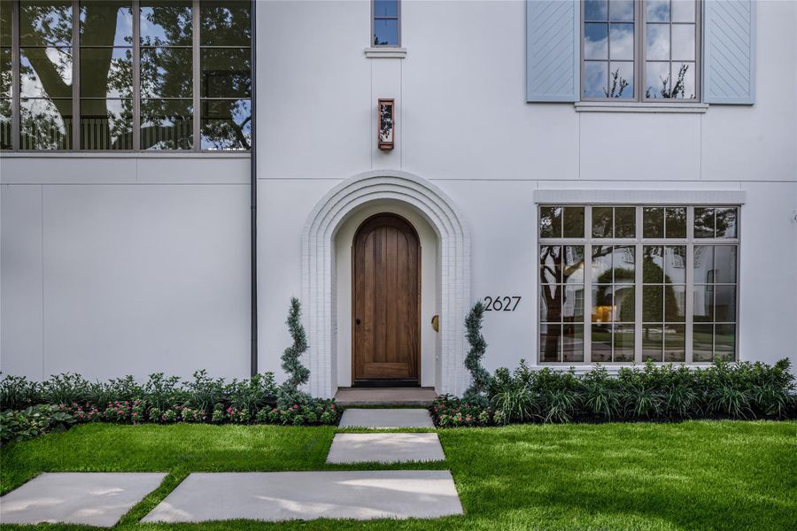 No one has called it home yet. The arched wood front door sits beneath layers of painted brick, framed by manicured landscaping and an oversized divided-light window that gives this just-completed home its unmistakable character.