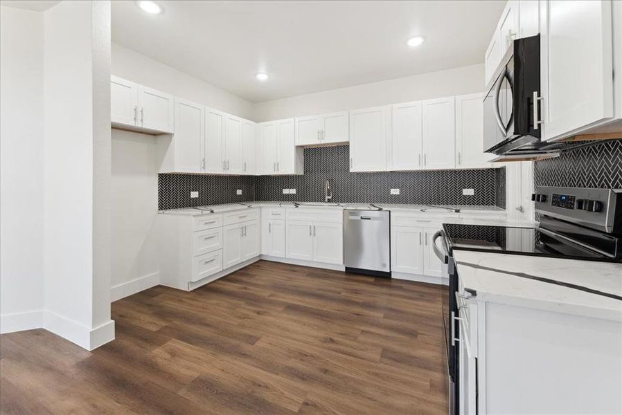 Kitchen featuring sink, backsplash,/ wood-style vinyl floors stainless steel appliances, and white cabinets, quartz counter tops