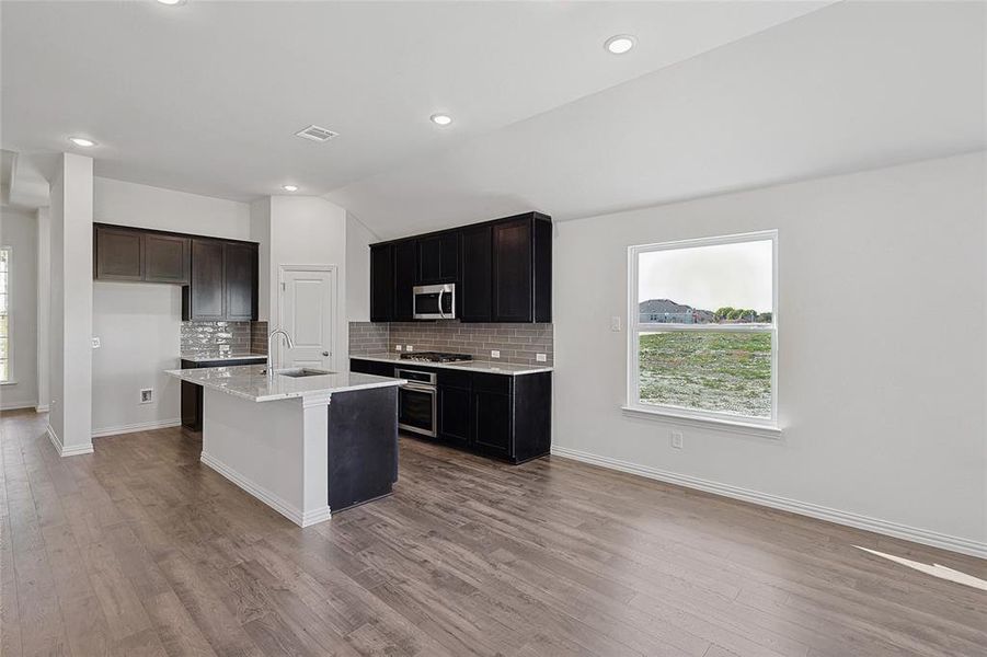 Kitchen featuring stainless steel appliances, light hardwood / wood-style flooring, a kitchen island with sink, and lofted ceiling