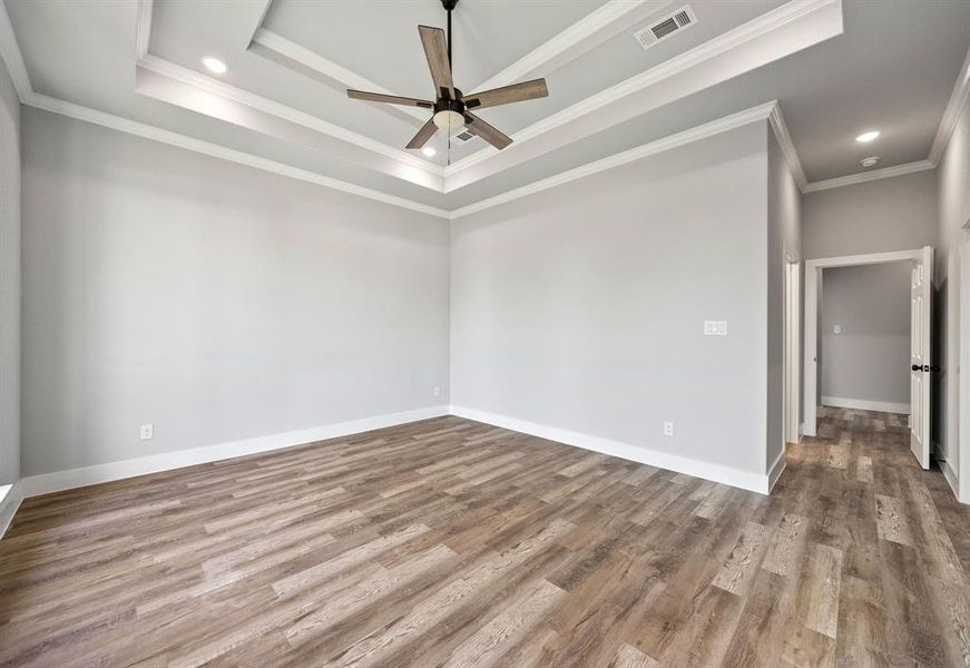 Empty room with a tray ceiling, ornamental molding, wood finished floors, a ceiling fan, and recessed lighting