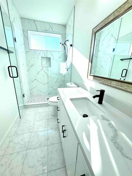 Full bath featuring vanity, light marble finish floors, and a marble finish shower