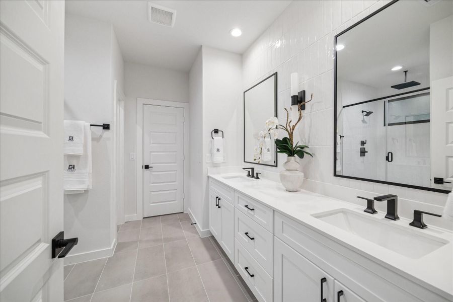Clean lines and contrast define this dual vanity with crisp white shaker cabinetry, quartz countertops, and matte black fixtures. Vertical tilework and oversized mirrors elevate the space with a polished, spa like feel.