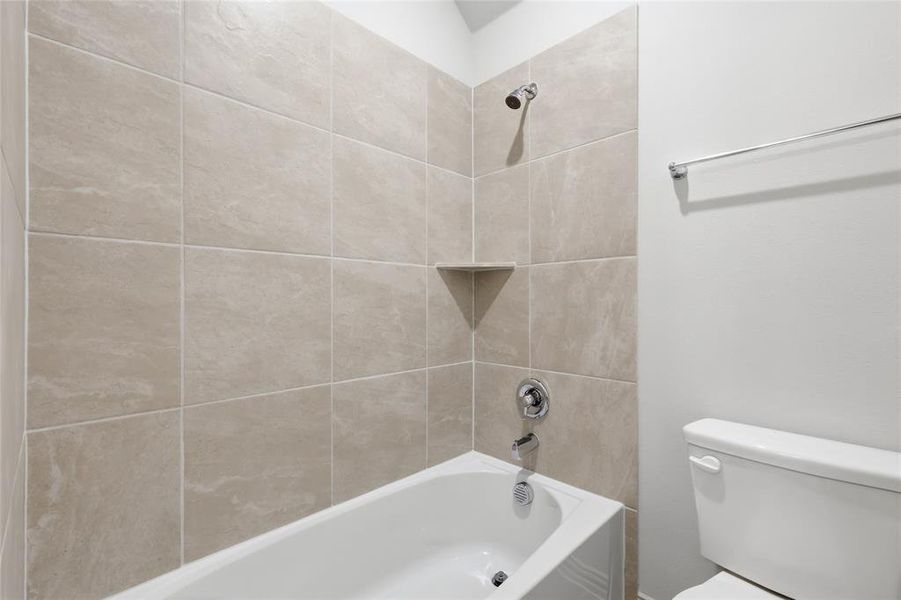 Bathtub and shower combination featuring neutral-toned tile surround with a corner shelf