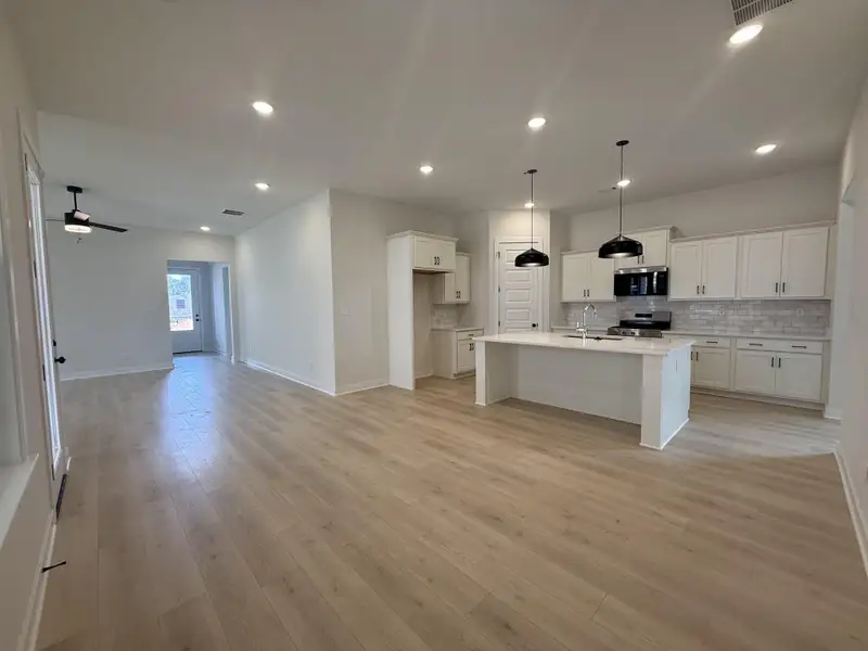 Kitchen featuring white cabinetry, open floor plan, an island with sink, stainless steel appliances, and hanging light fixtures