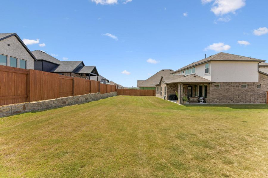 A spacious grassy lawn bordered by wooden fencing and stone retaining walls under blue skies.