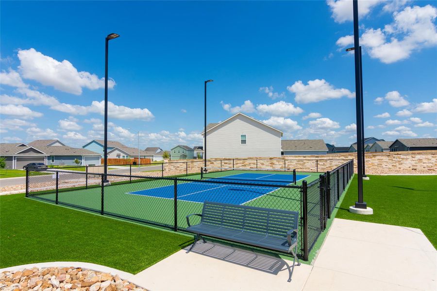 Fenced court featuring a blue playing surface with white lines, surrounded by green turf
