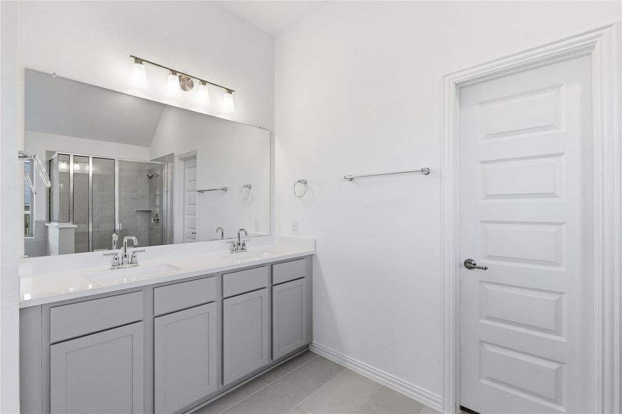 Full bath featuring a stall shower, double vanity, and light tile patterned flooring