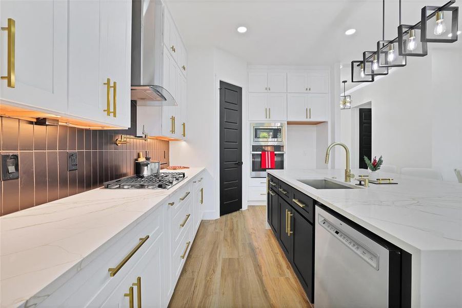 Kitchen featuring stainless steel appliances, a sink, wall chimney exhaust hood, white cabinetry, and light wood-style flooring