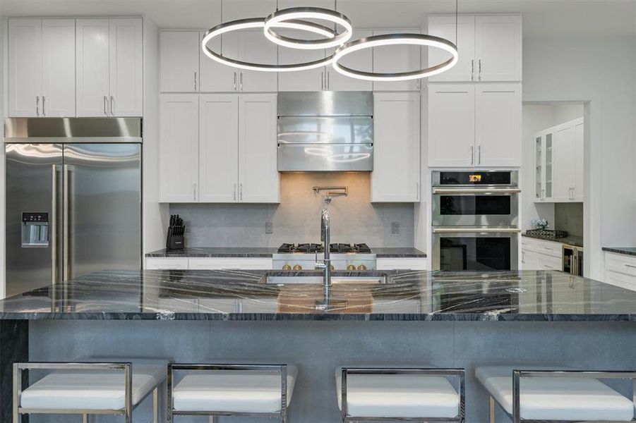 Kitchen with a kitchen bar, stainless steel appliances, dark stone counters, white cabinets, and range hood Kitchen with a kitchen bar, stainless steel appliances, dark stone counters, white cabinets, and range hood