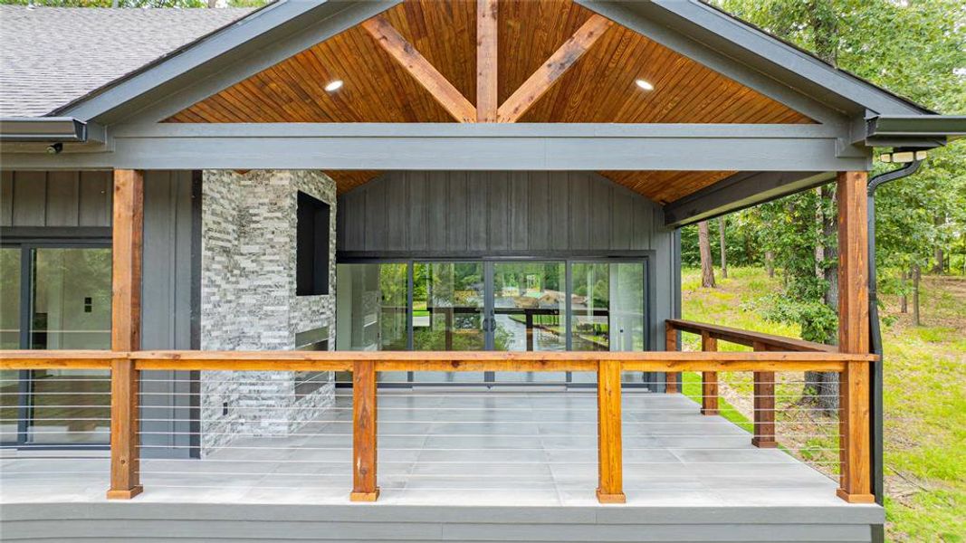 Covered outdoor living space featuring a wood-planked vaulted ceiling, recessed lighting, and a stone-clad fireplace