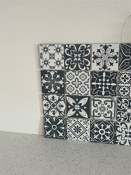 This is a modern kitchen backsplash featuring a monochrome, decorative tile design with a variety of intricate patterns, set against a clean, light-colored countertop and a neutral wall, offering a stylish and contemporary look.