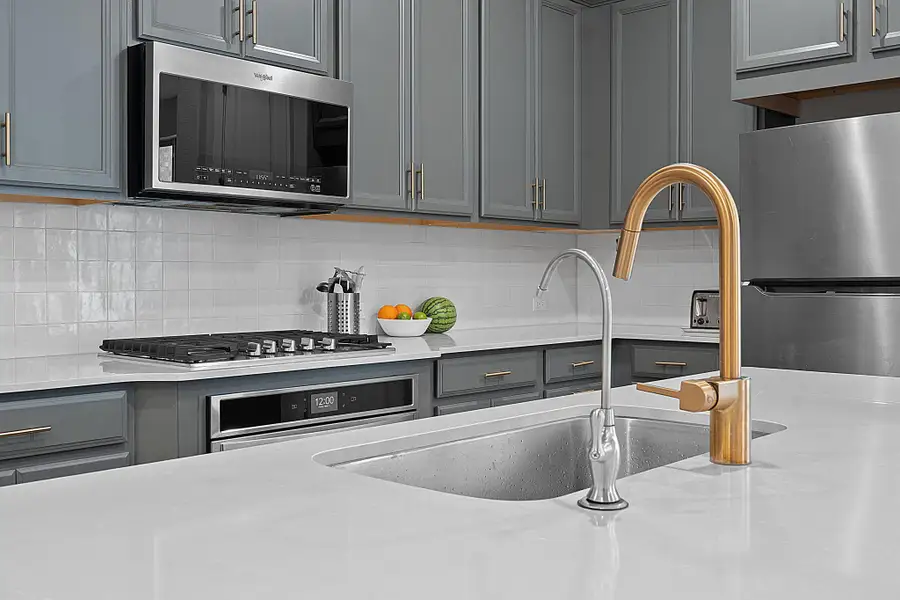 Kitchen featuring gray cabinetry, appliances with stainless steel finishes, tasteful backsplash, and light stone counters Kitchen featuring gray cabinetry, appliances with stainless steel finishes, tasteful backsplash, and light stone counters