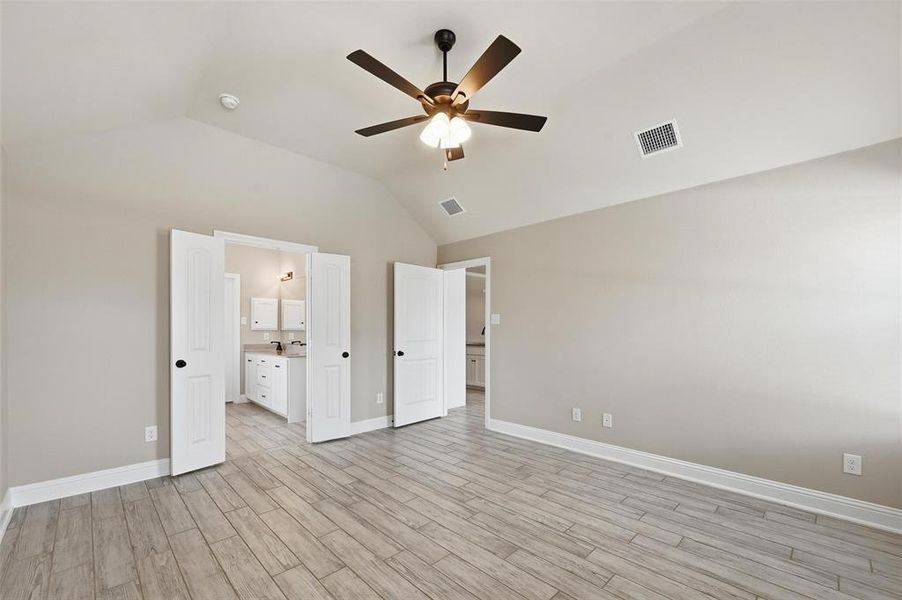Unfurnished bedroom featuring light wood-style floors, a ceiling fan, vaulted ceiling, and connected bathroom Unfurnished bedroom featuring light wood-style floors, a ceiling fan, vaulted ceiling, and connected bathroom