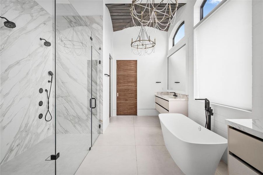 The primary bathroom showcases stunning natural stone finishes and a spacious glass-enclosed shower. The freestanding soaking tub adds a touch of modern elegance and is complemented by dual vanities for ample storage and convenience.