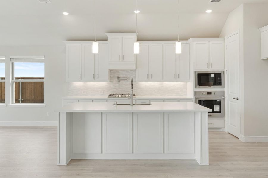 White kitchen with large island, pendant lights, tile backsplash, and stainless steel built-in appliances