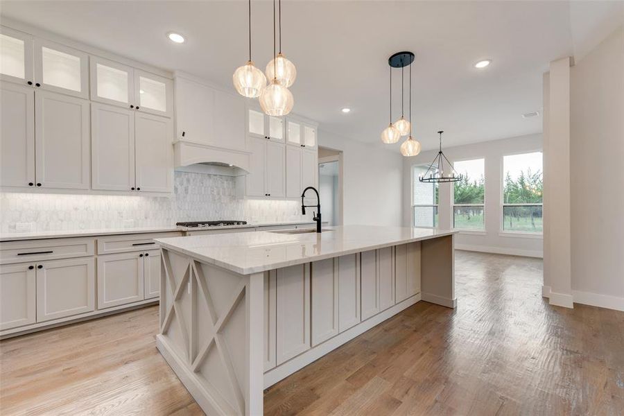 Kitchen with sink, white cabinetry, light wood-type flooring, and a kitchen island with sink