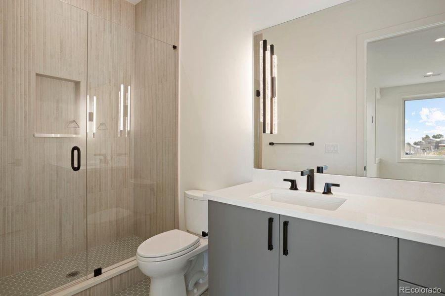 En suite bath to Bedroom 2 featuring a frameless glass shower, sleek vertical tile, and a modern vanity with black fixtures.