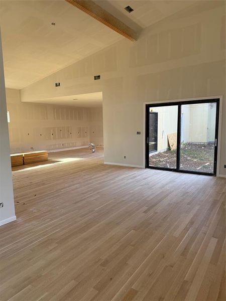 Empty room featuring beam ceiling, light wood-style flooring, and high vaulted ceiling Empty room featuring beam ceiling, light wood-style flooring, and high vaulted ceiling