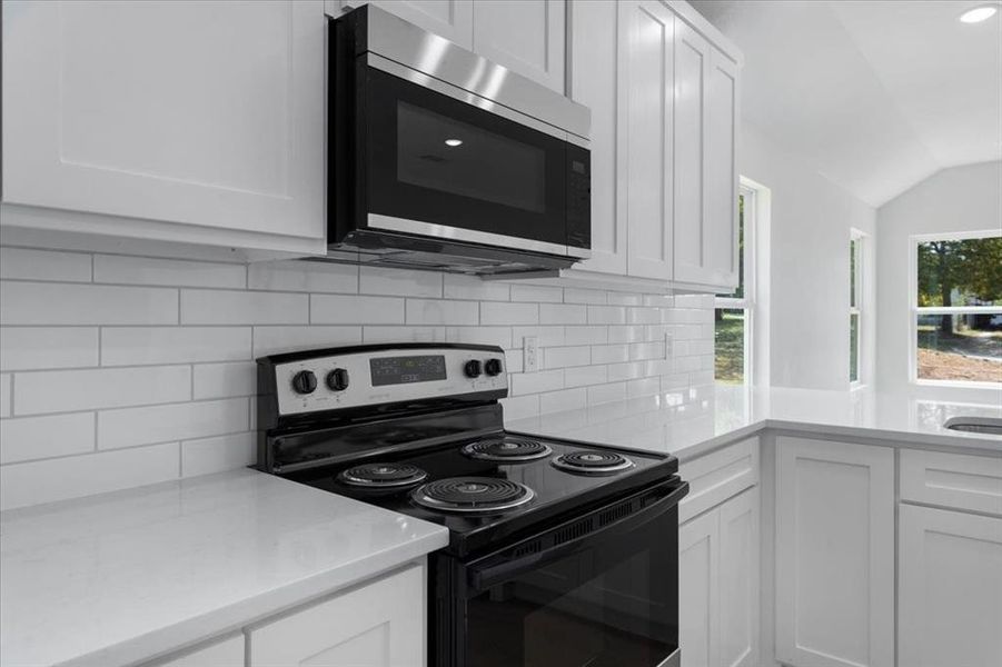 Kitchen with white cabinetry, backsplash, vaulted ceiling, and stainless steel appliances