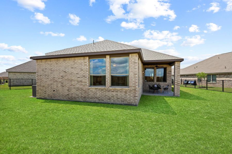Expansive backyard featuring a manicured lawn, brick exterior, covered patio, and black metal fencing