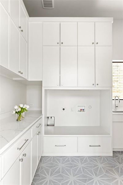 Bright utility space featuring extensive white cabinetry, a built-in appliance alcove, a spacious countertop, and geometric patterned floor tiling