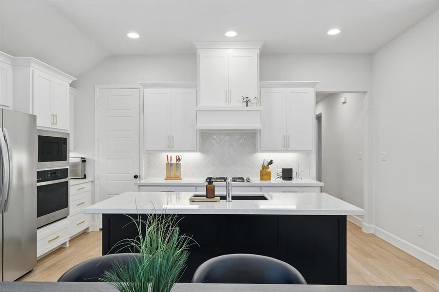 Kitchen featuring stainless steel appliances, a center island with sink, white cabinets, and light countertops