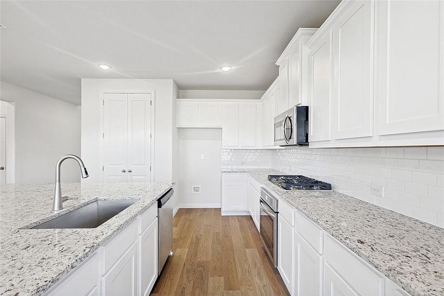 Kitchen with light wood-style flooring, white cabinetry, light stone countertops, stainless steel appliances, and recessed lighting Kitchen with light wood-style flooring, white cabinetry, light stone countertops, stainless steel appliances, and recessed lighting