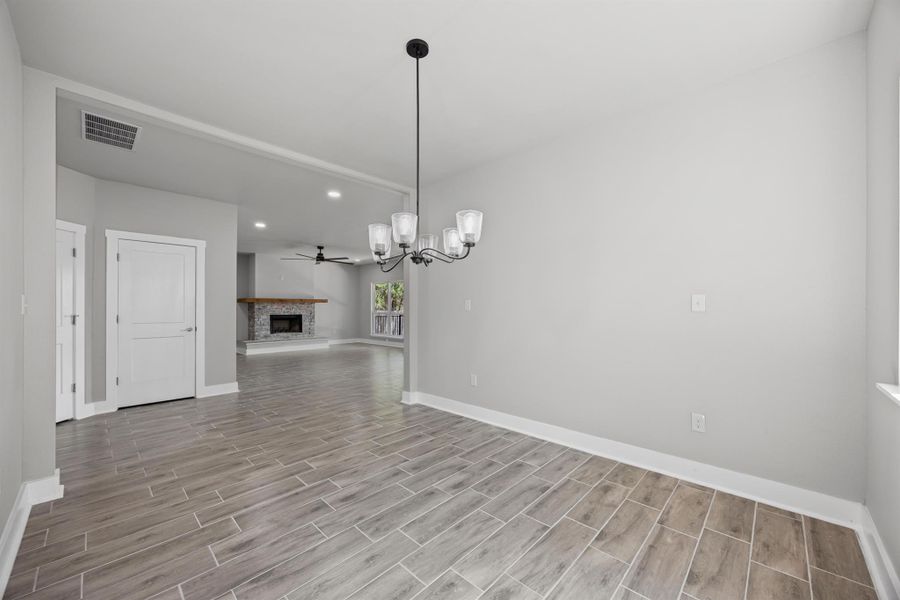 Unfurnished dining area with a chandelier, a fireplace with raised hearth, a ceiling fan, wood finish floors, and recessed lighting Unfurnished dining area with a chandelier, a fireplace with raised hearth, a ceiling fan, wood finish floors, and recessed lighting