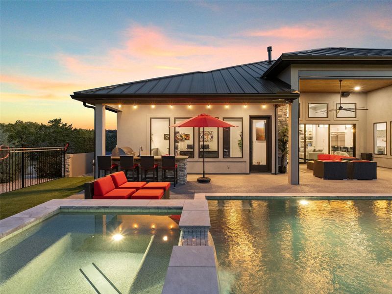 Back of property at dusk featuring an outdoor lounge area with bar, a patio area, a jacuzzi, stucco siding, and a standing seam roof