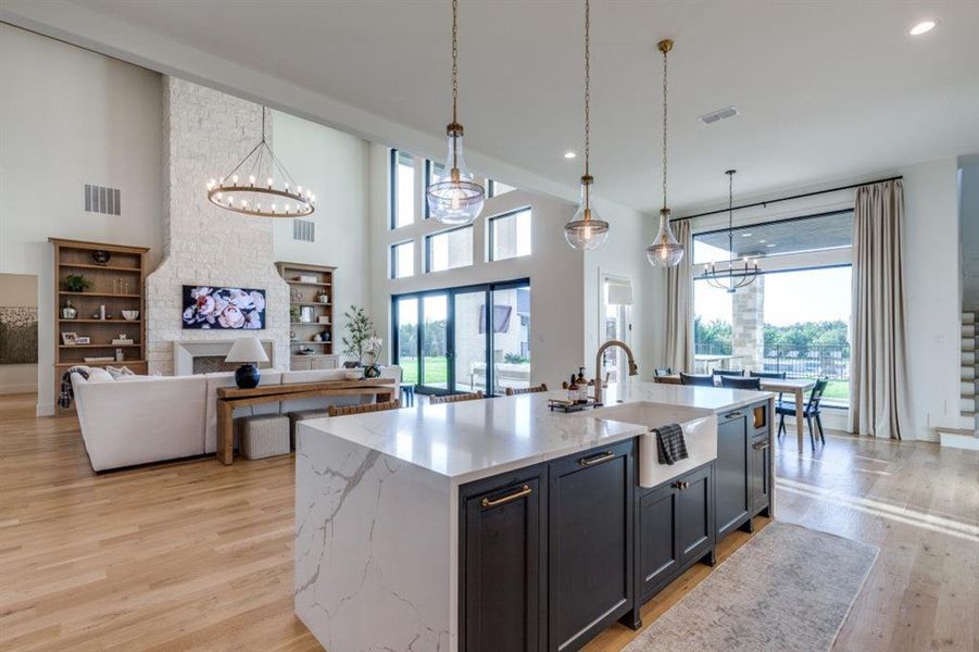 Kitchen featuring a chandelier, light wood-style floors, light stone counters, a kitchen island with sink, and pendant lighting Kitchen featuring a chandelier, light wood-style floors, light stone counters, a kitchen island with sink, and pendant lighting