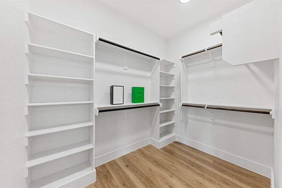 Walk-in closet with built-in shelving, hanging rods, and hardwood style flooring Walk-in closet with built-in shelving, hanging rods, and hardwood style flooring
