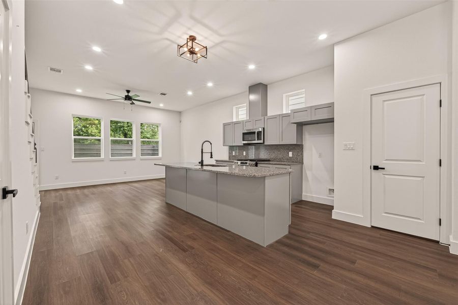 This photo showcases a modern, open-concept kitchen and living area with sleek engineer wood floors, neutral walls, and ample natural light from multiple windows. The kitchen features a large island with granite countertops, stainless steel appliances, and stylish gray cabinetry, perfect for entertaining and everyday living. This photo showcases a modern, open-concept kitchen and living area with sleek engineer wood floors, neutral walls, and ample natural light from multiple windows. The kitchen features a large island with granite countertops, stainless steel appliances, and stylish gray cabinetry, perfect for entertaining and everyday living.