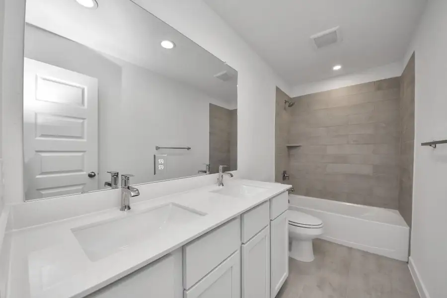 Secondary bath features tile flooring, bath/shower combo with tile surround, light stained wood cabinets, beautiful light countertop. Sample photo of completed home with similar floor plan. Actual colors and selections may vary.