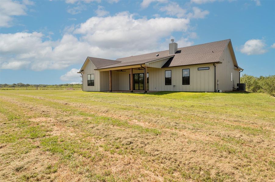 Back of property featuring a patio area, a shingled roof, a chimney, a lawn, and a ceiling fan