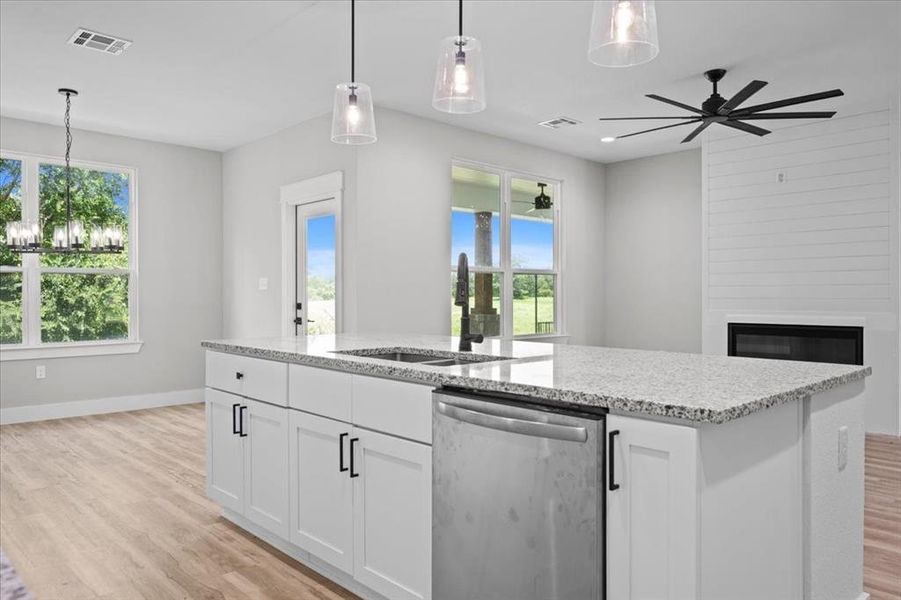Kitchen with stainless steel dishwasher, light wood-style flooring, open floor plan, light stone counters, and ceiling fan