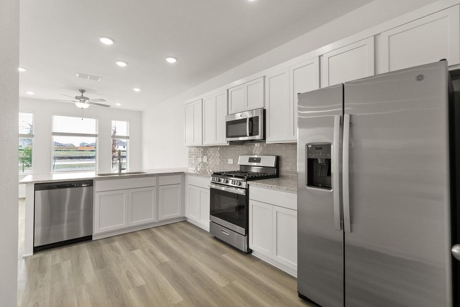 Kitchen with stainless steel appliances, white cabinets, light wood-type flooring, recessed lighting, and decorative backsplash