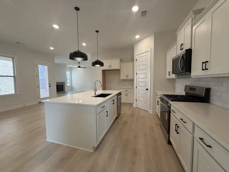 Kitchen featuring stainless steel appliances, a kitchen island with sink, white cabinets, and a fireplace