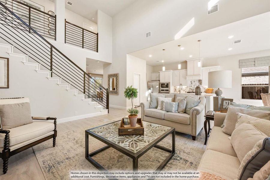 Open-concept living room with two-story ceiling, staircase, and view into kitchen with white cabinets